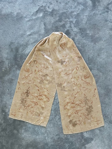 natural dye silk charmeuse scarf in pale bronze color with brown and rust color eco print patterns on a concrete ground